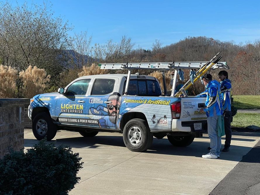 Blue advertising truck parked on a driveway with two people standing beside it in a sunny outdoor area