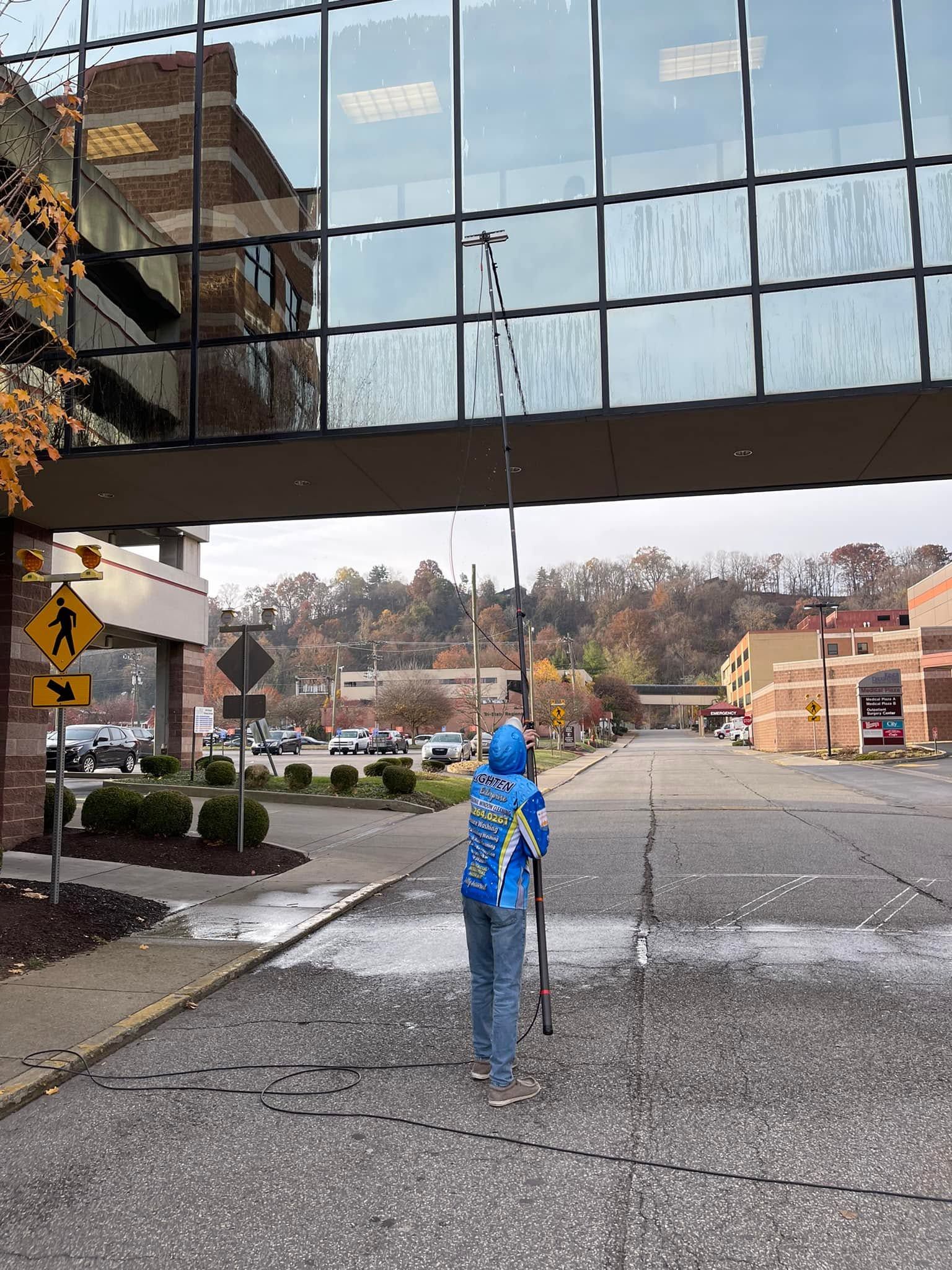 Person in blue hoodie standing on a wet street beneath a glass building overhang.