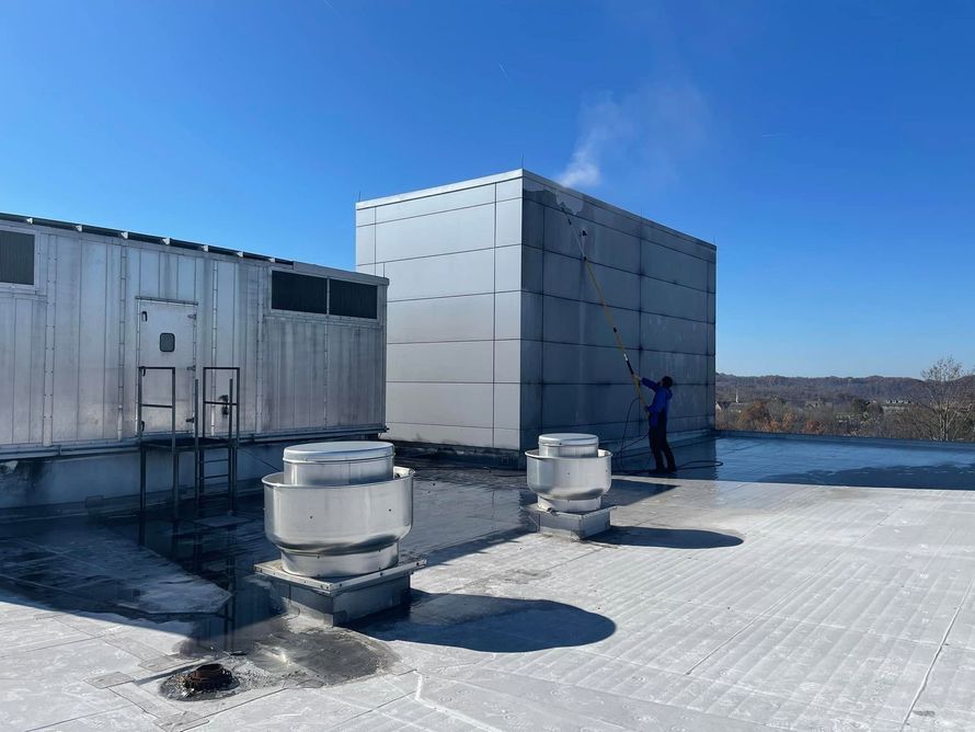 Rooftop with HVAC units and a person standing near a large white equipment enclosure by the water