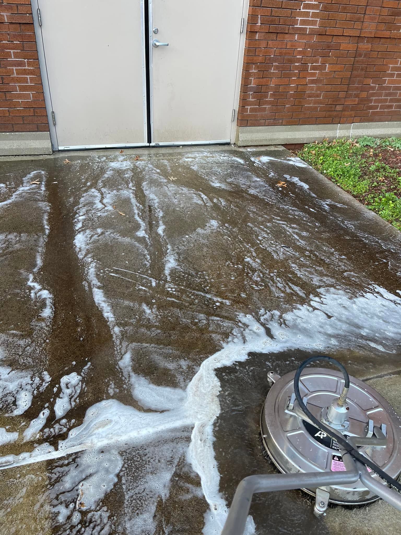 Snow-dusted concrete patio beside a brick building, with a metal chair in the foreground.