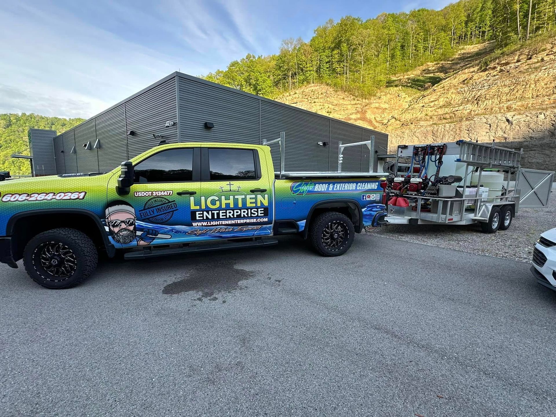 Blue Lichten Customs truck with a racing trailer parked on gravel beside a hillside.
