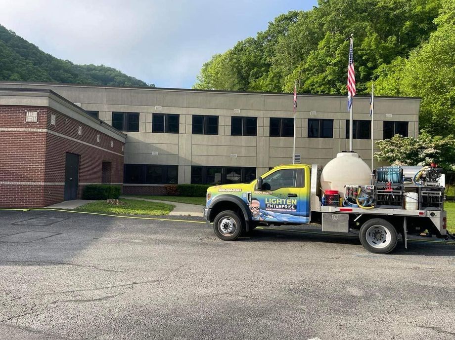 Yellow utility truck parked in front of a beige building with trees and a flagpole