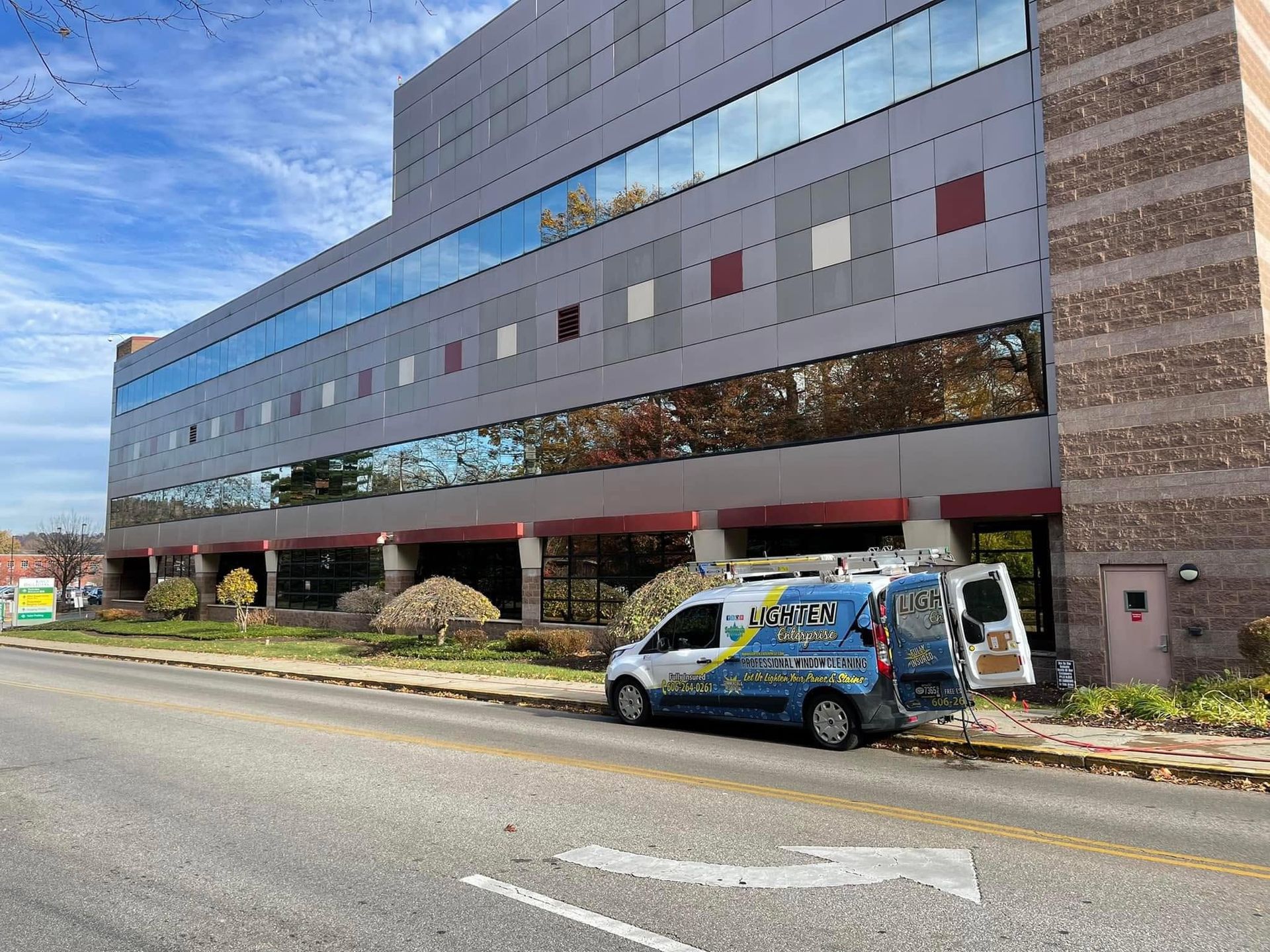 A modern office building beside a street, with a parked blue service van in front.