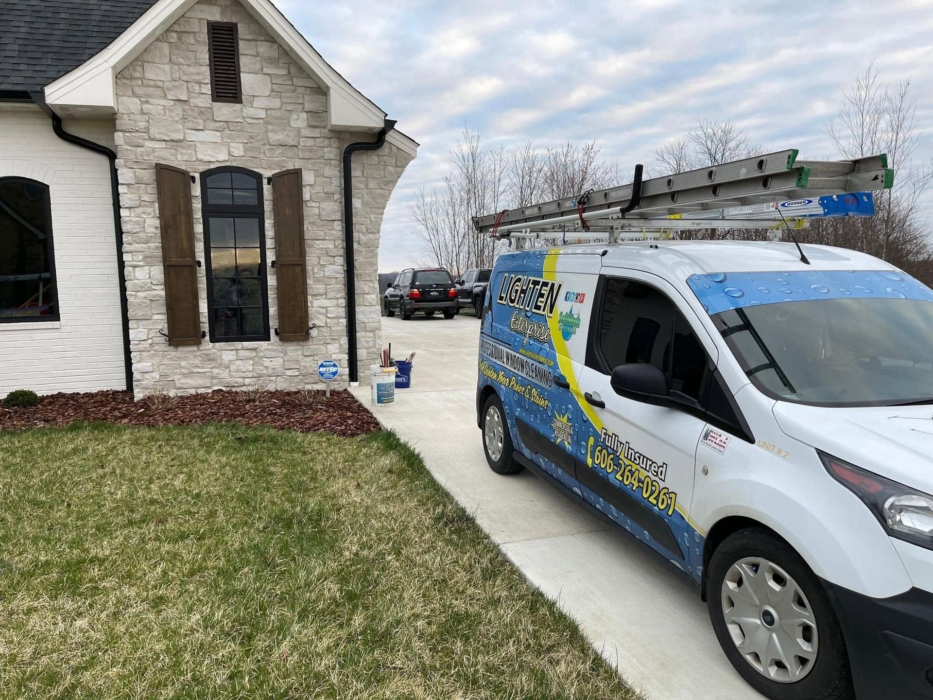 Service van parked in a driveway beside a stone house on a grassy lawn.