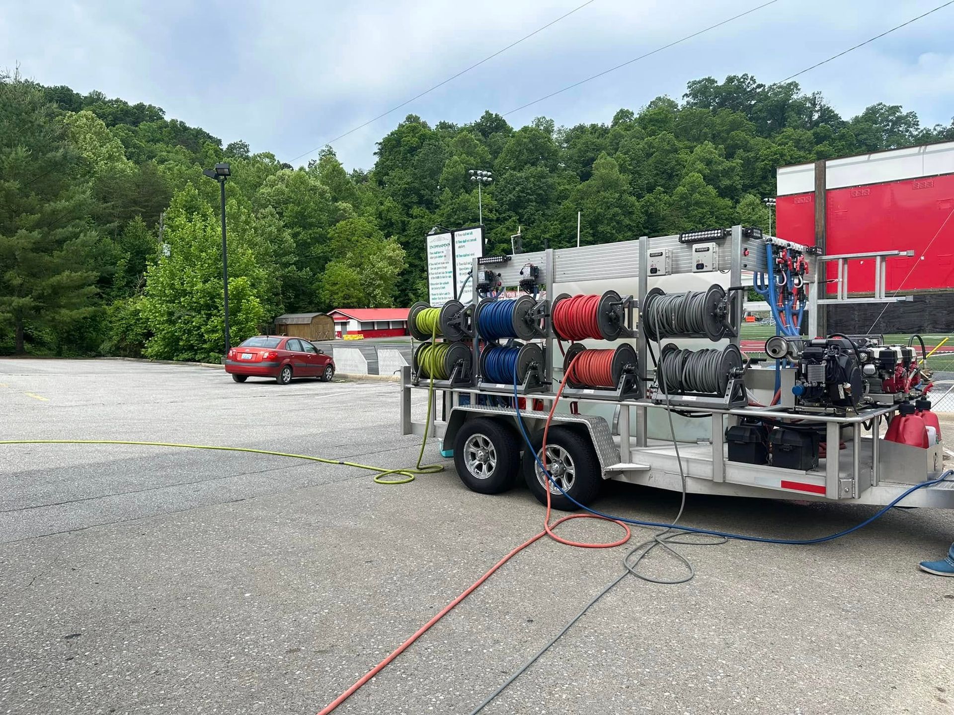 Fire hose truck trailer with coiled hoses parked on a gravel lot near trees and a red building