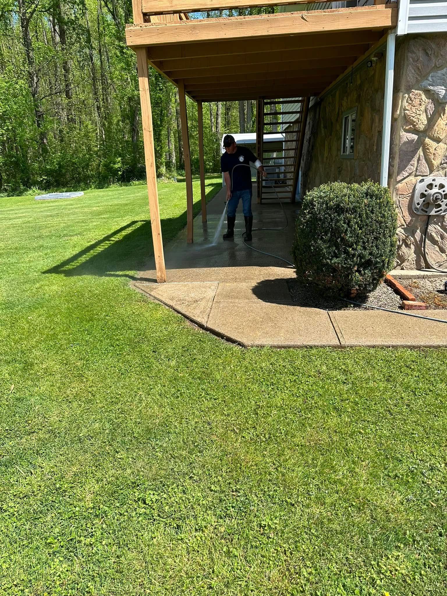 Person standing under a wooden deck beside a house, with green lawn and shrubs nearby