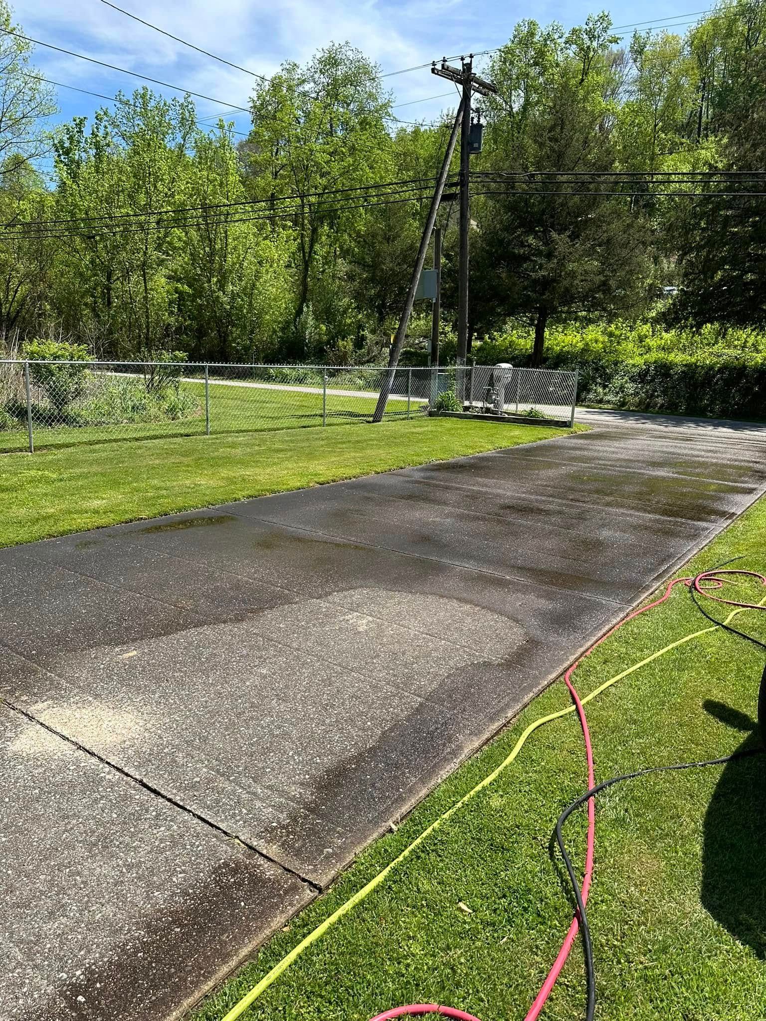 Cracked concrete driveway beside green lawn and trees, with a red hose along the edge