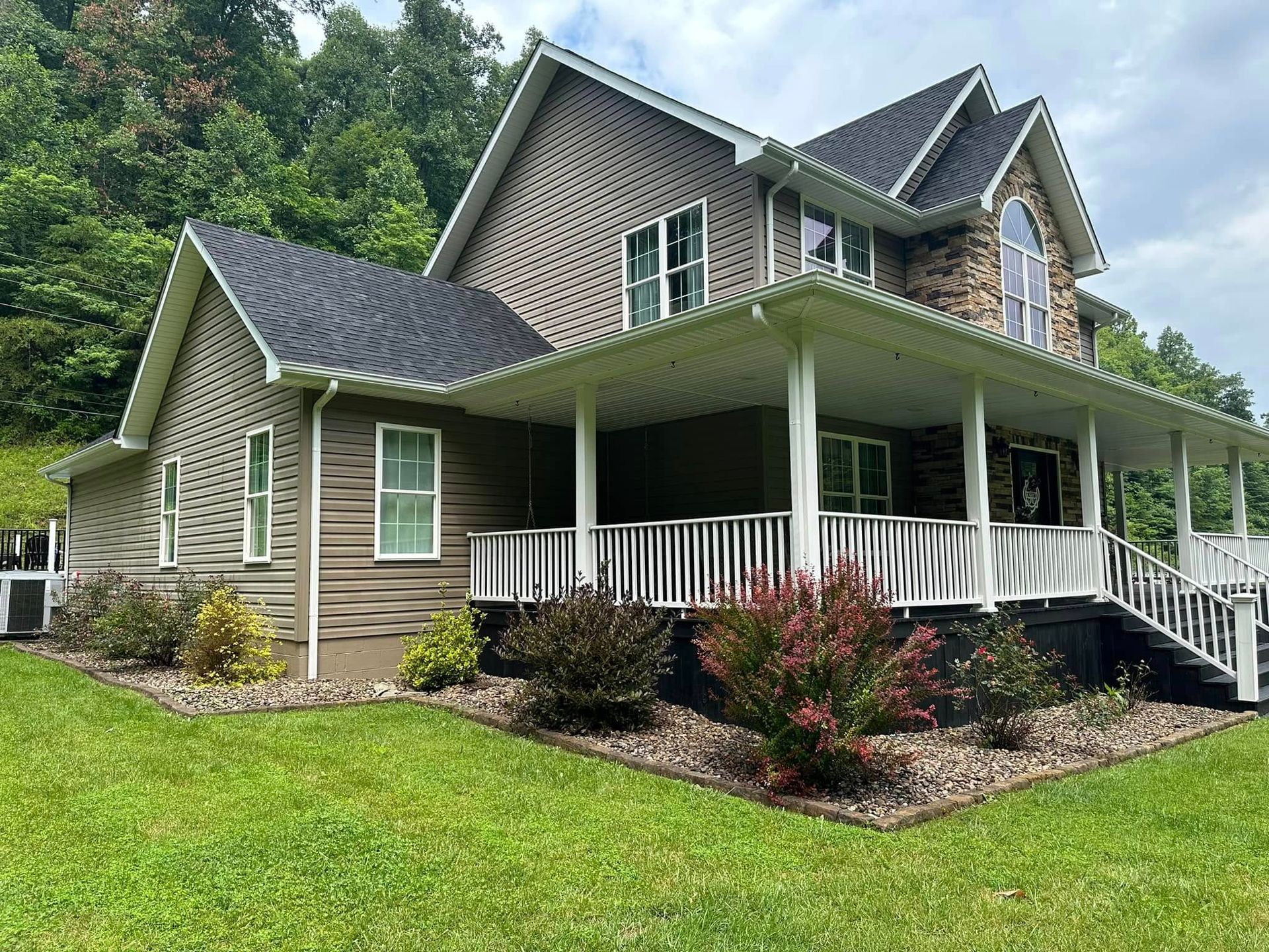 Modern gray house with a large wraparound porch, gabled roof, and landscaped green lawn.