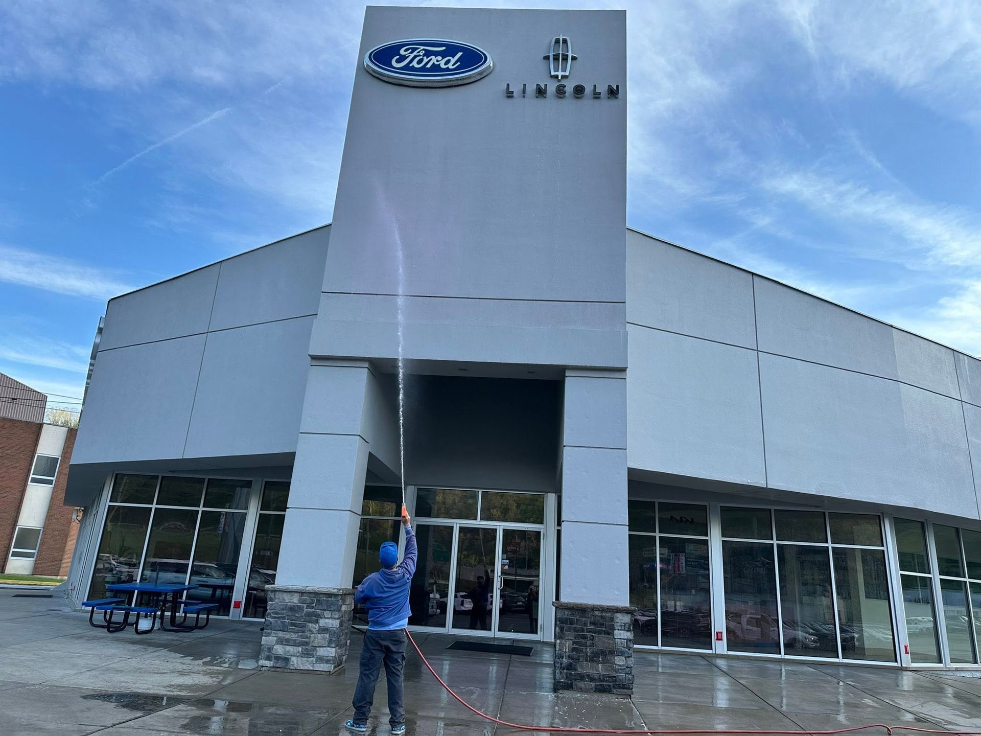 Ford dealership exterior with large logo, glass windows, and a person holding a pole in front