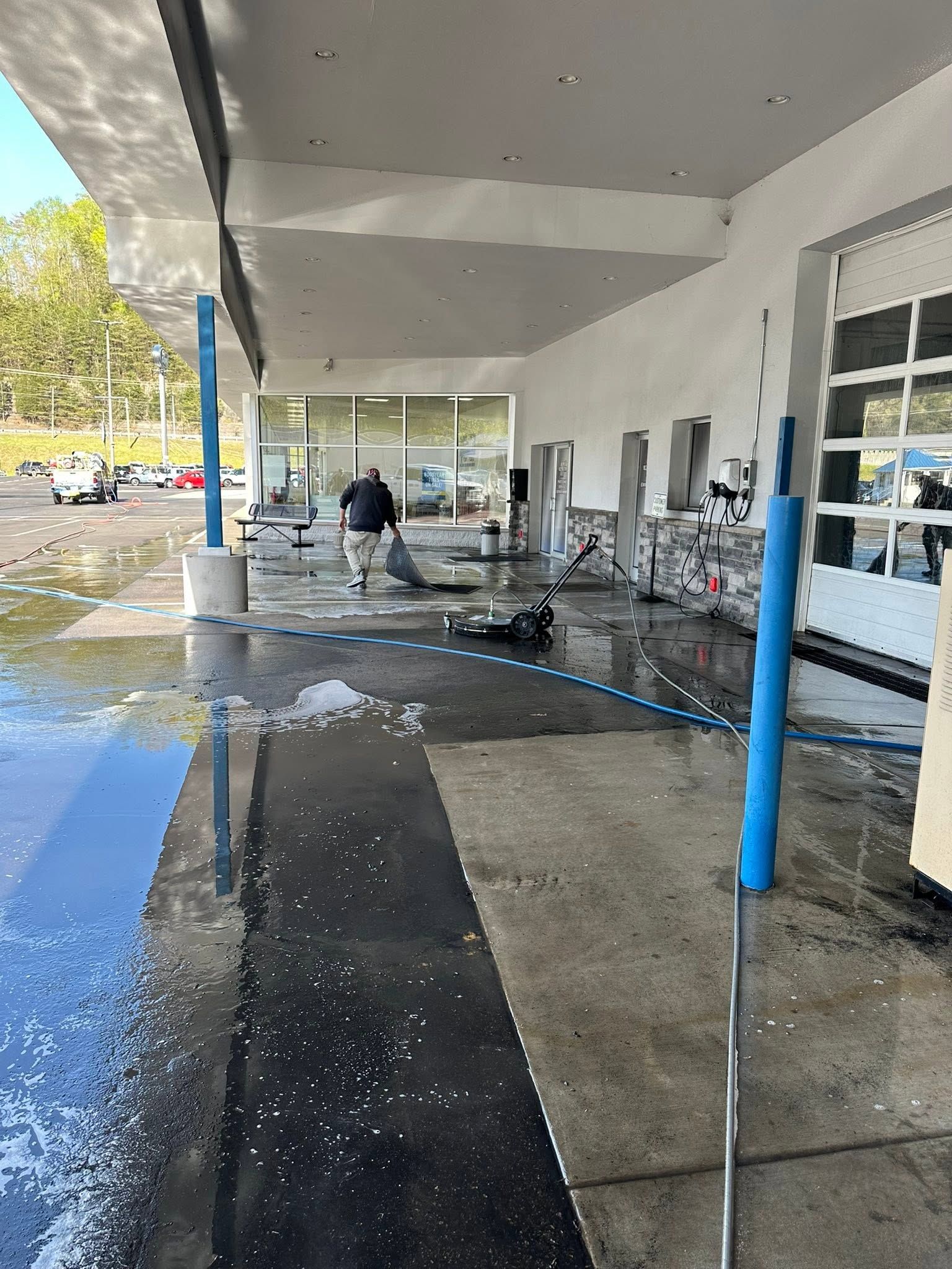Person pressure-washing a covered storefront walkway with blue support poles.