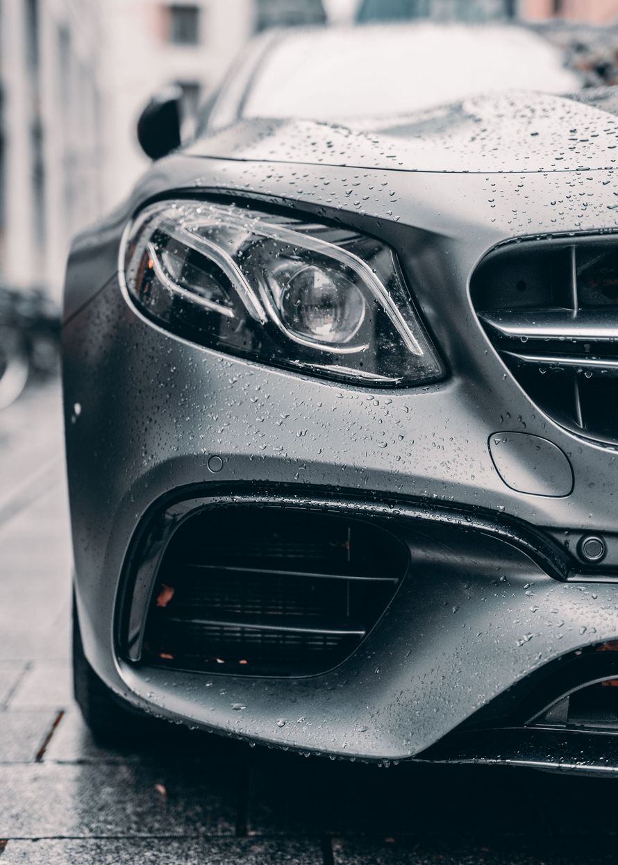 Close-up of a silver sports car front end with raindrops, parked on a wet street.