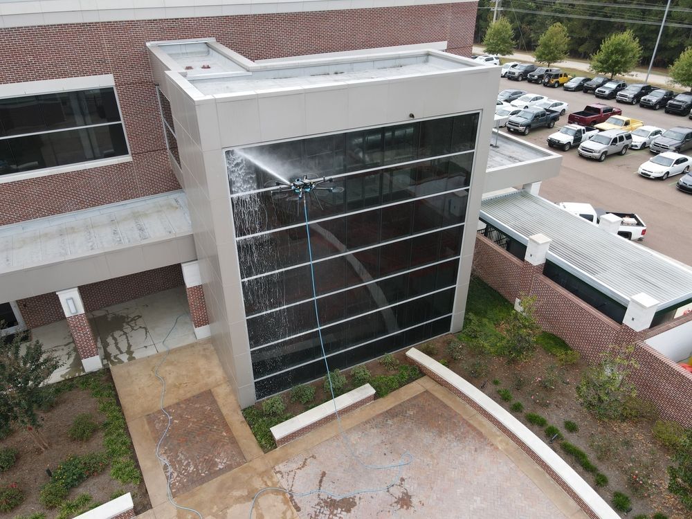Aerial view of a modern building entrance with a glass facade, brick walls, and surrounding parking lot.