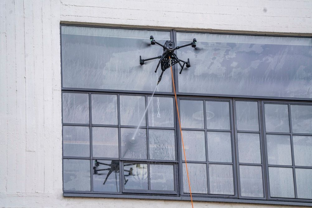 Drone cleaning a large industrial window on a building facade