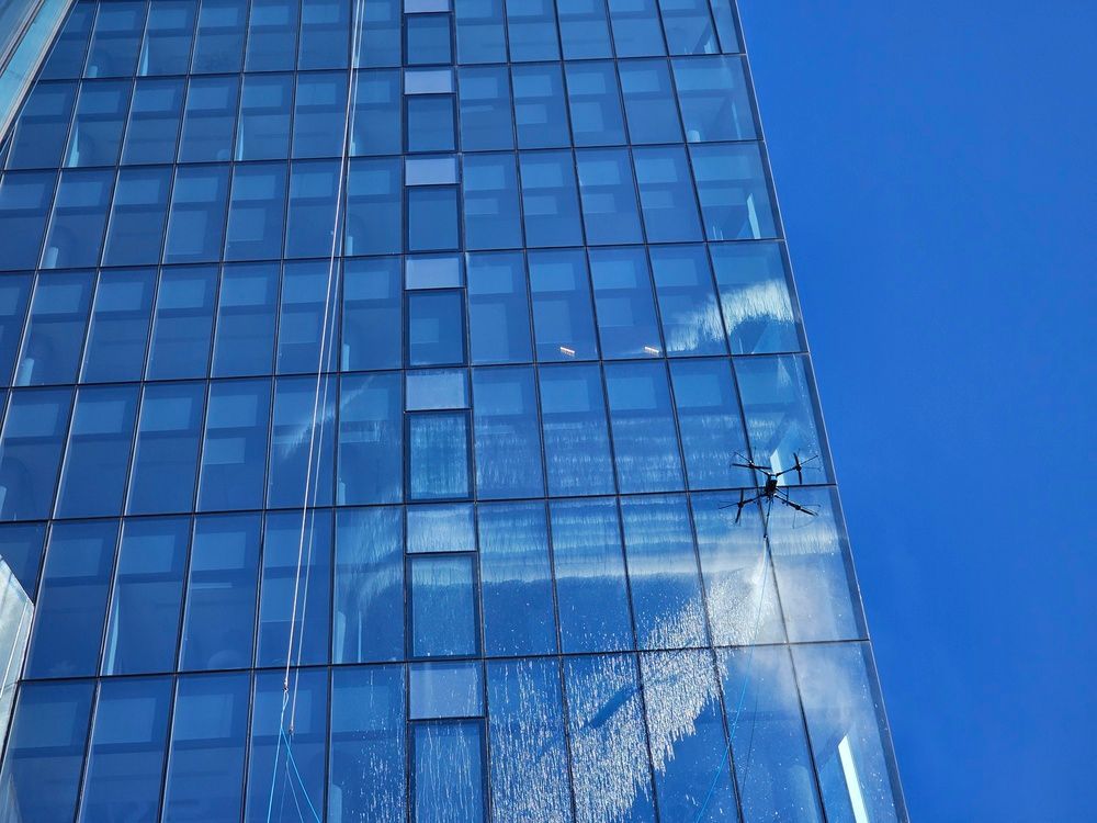 Glass office building facade reflecting blue sky and clouds, with a drone flying near the windows