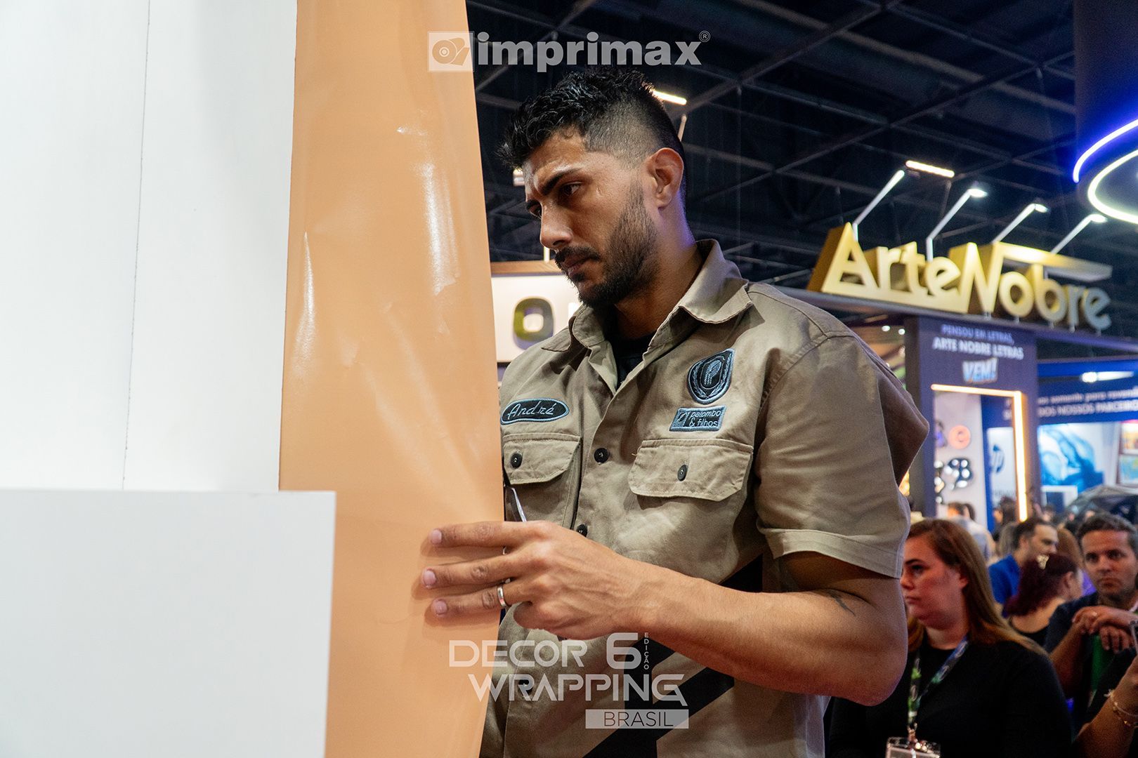 Um instalador profissional aplica uma película de vinil cor de pêssego em uma superfície em um estande de feira comercial.