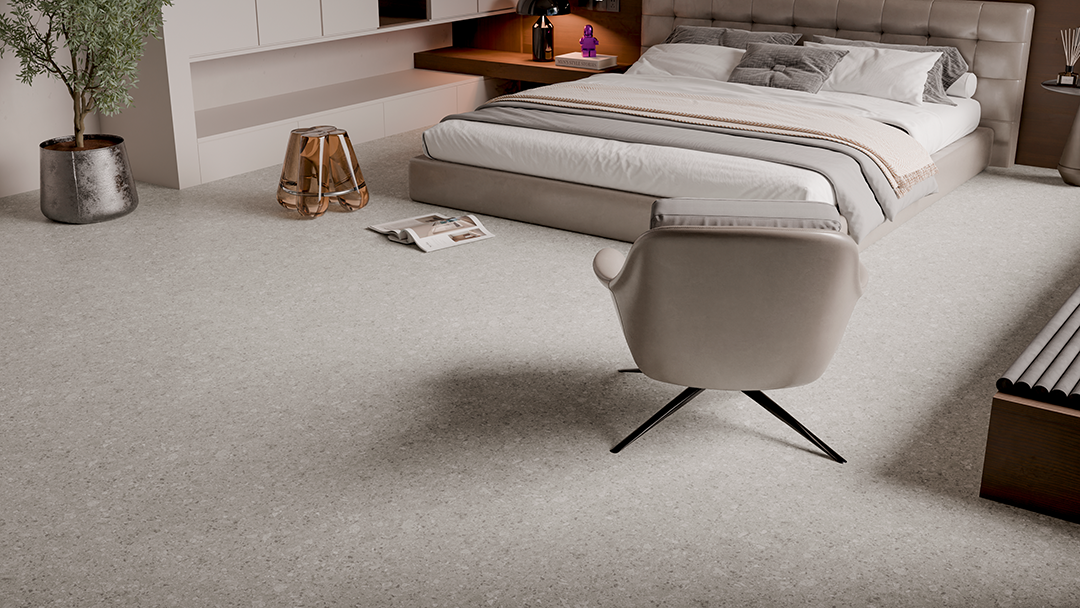 Um quarto com carpete claro, uma cama grande com roupa de cama neutra, uma cadeira giratória e uma mesa de cabeceira decorativa dourada.
