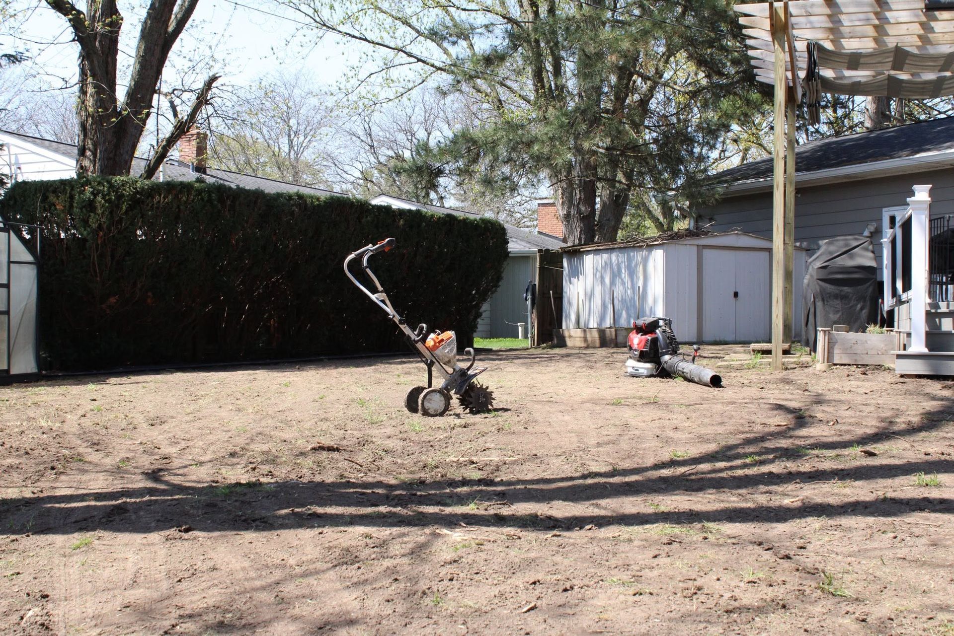 Backyard with bare trees, a wheelbarrow, and a child’s scooter on dirt ground near a garage