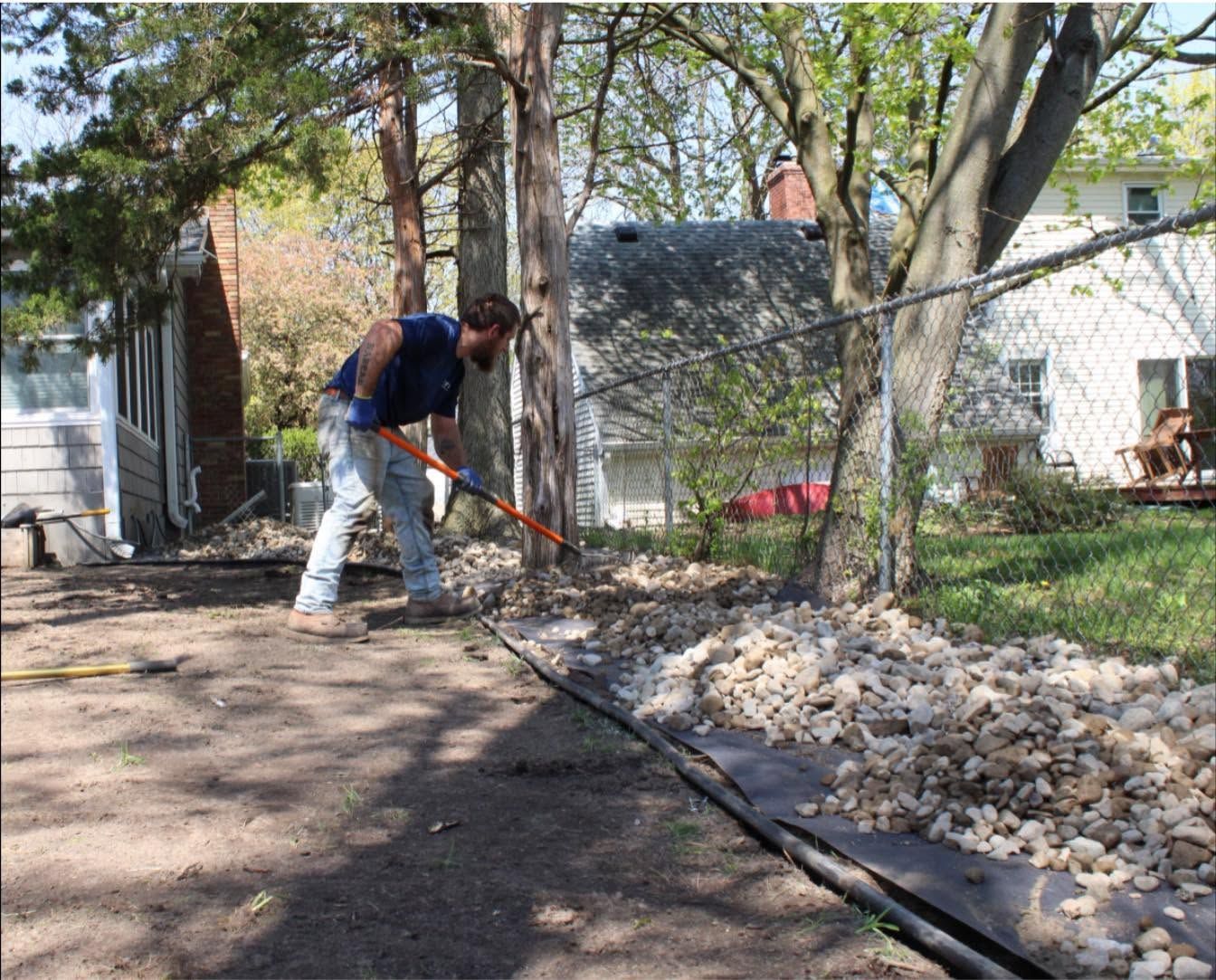 Worker using a rake to clear debris along a fence in a wooded yard