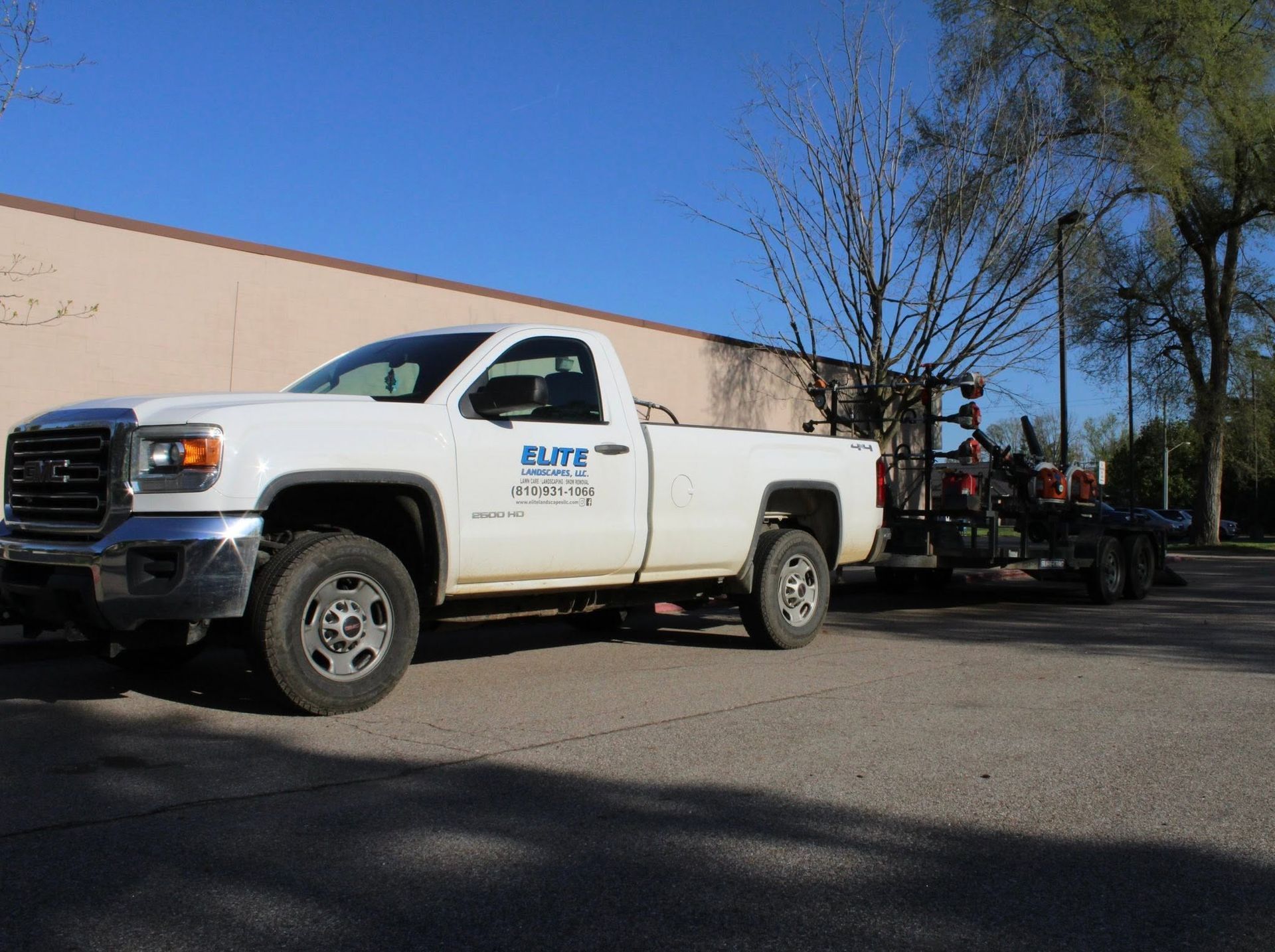 White pickup truck with a trailer parked on a sunny street beside a building