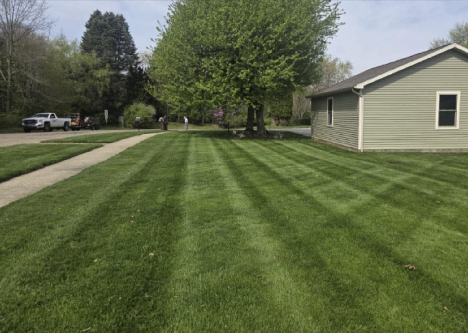 Neatly mowed green lawn beside a beige house and driveway on a cloudy day.