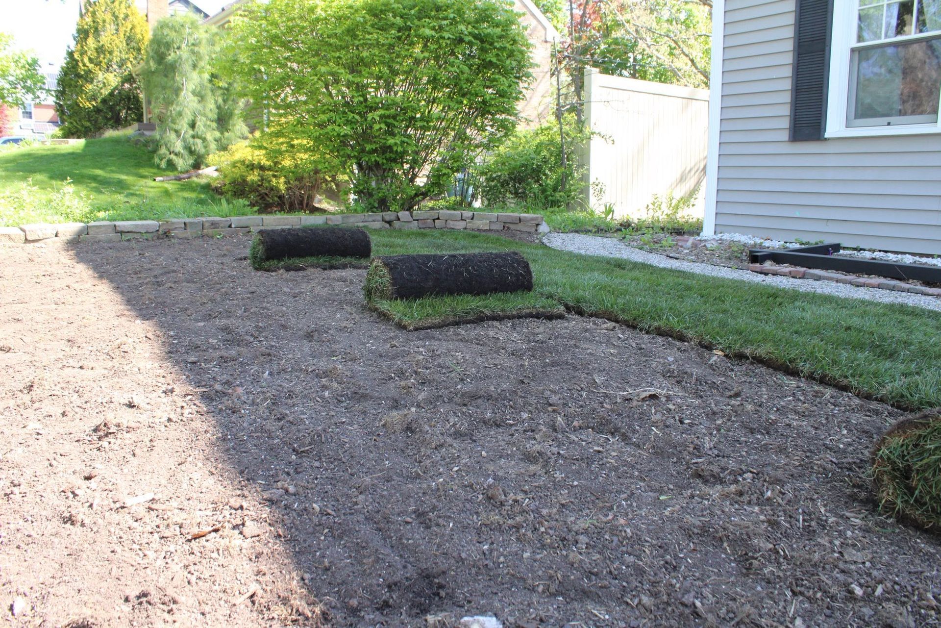 Freshly mulched garden bed beside a house with rolled sod and green shrubs in the background
