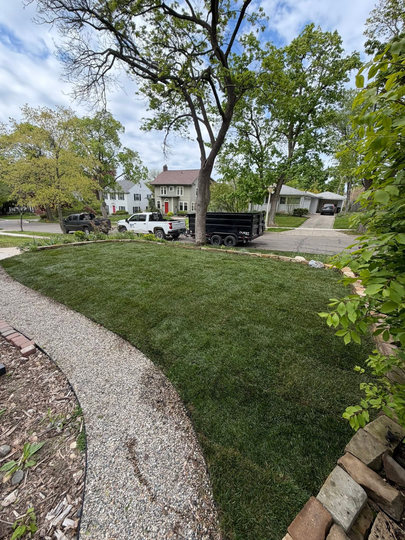 Curved stone path beside a green lawn and trees, leading to a house and parked car on a sunny day