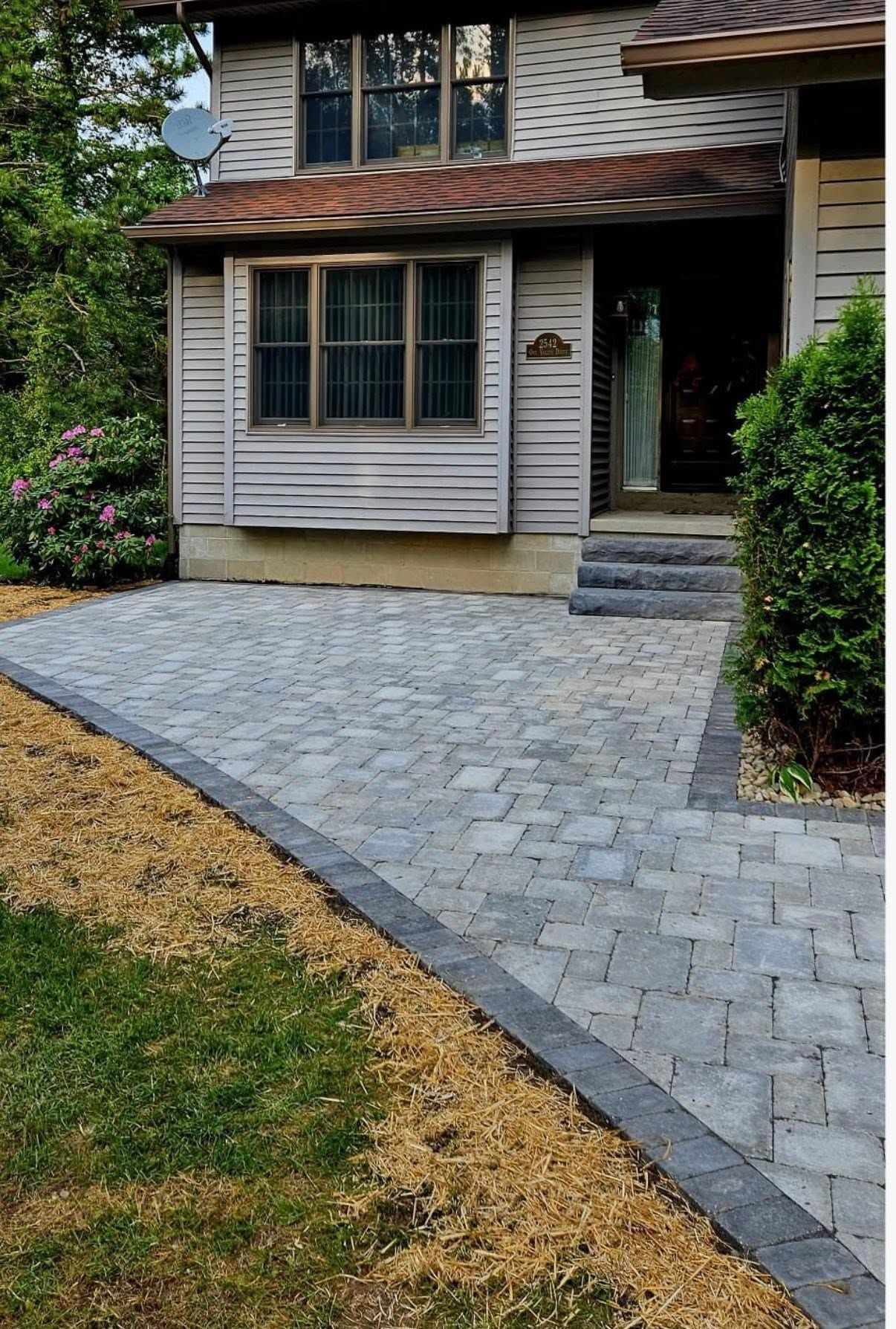 Stone paver walkway leading to a front porch with a tan house and shrubs on either side