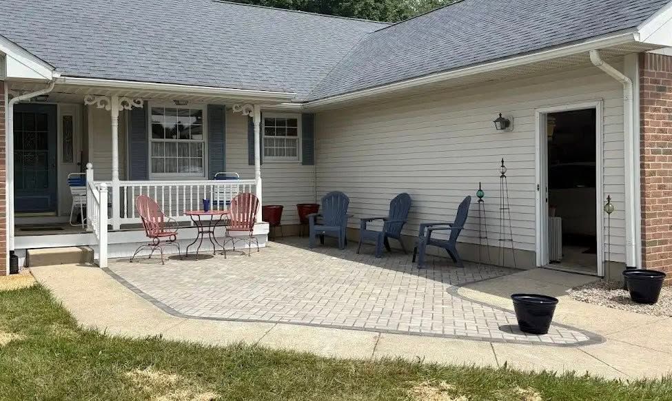 Patio with red and blue chairs, small table, and potted plants beside a beige house