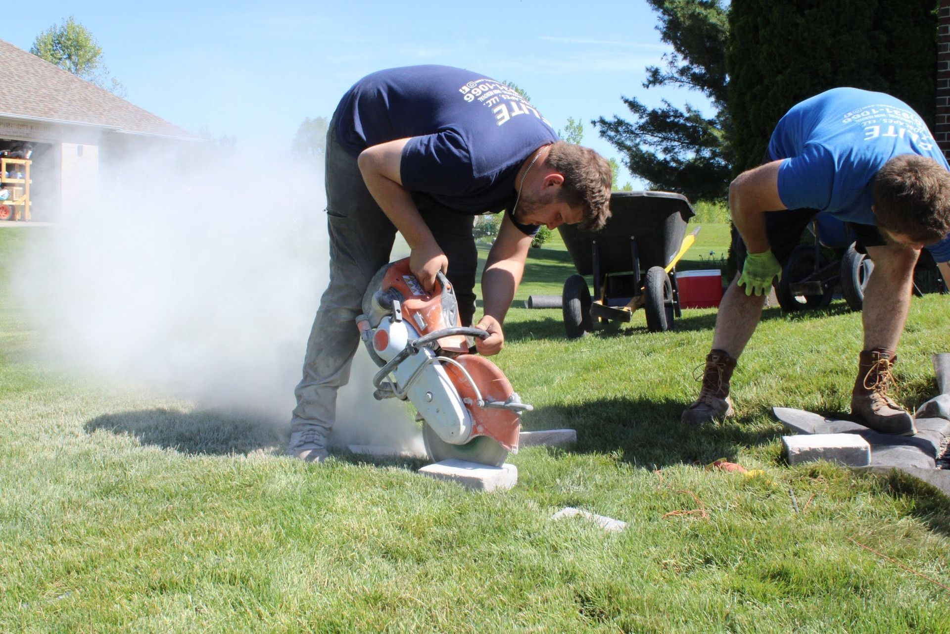 Two people using circular saws outdoors, with one kicking up a cloud of sawdust on a sunny lawn.