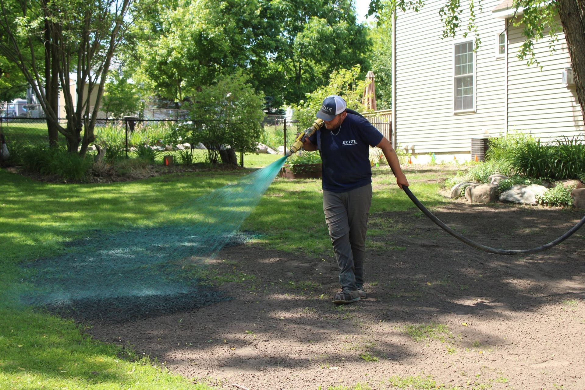 Person watering a lawn with a hose beside a house on a sunny day