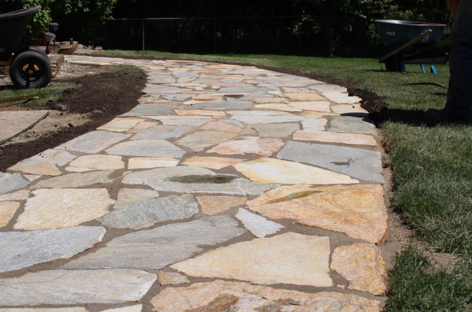 Curved stone walkway beside grass in a yard with a wheelbarrow in the distance