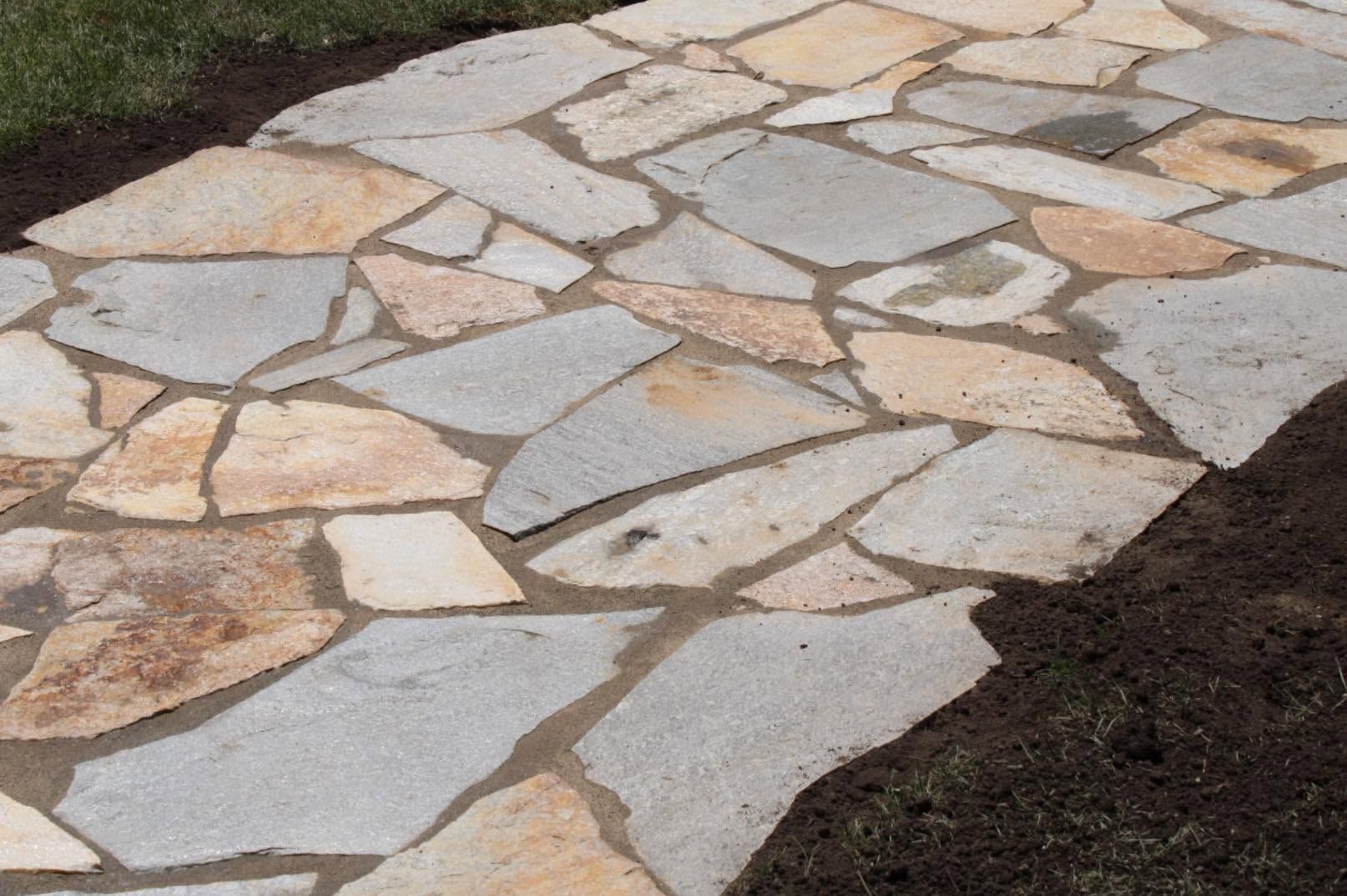Irregular tan and gray stone pavers set in dark soil, forming a decorative path outdoors
