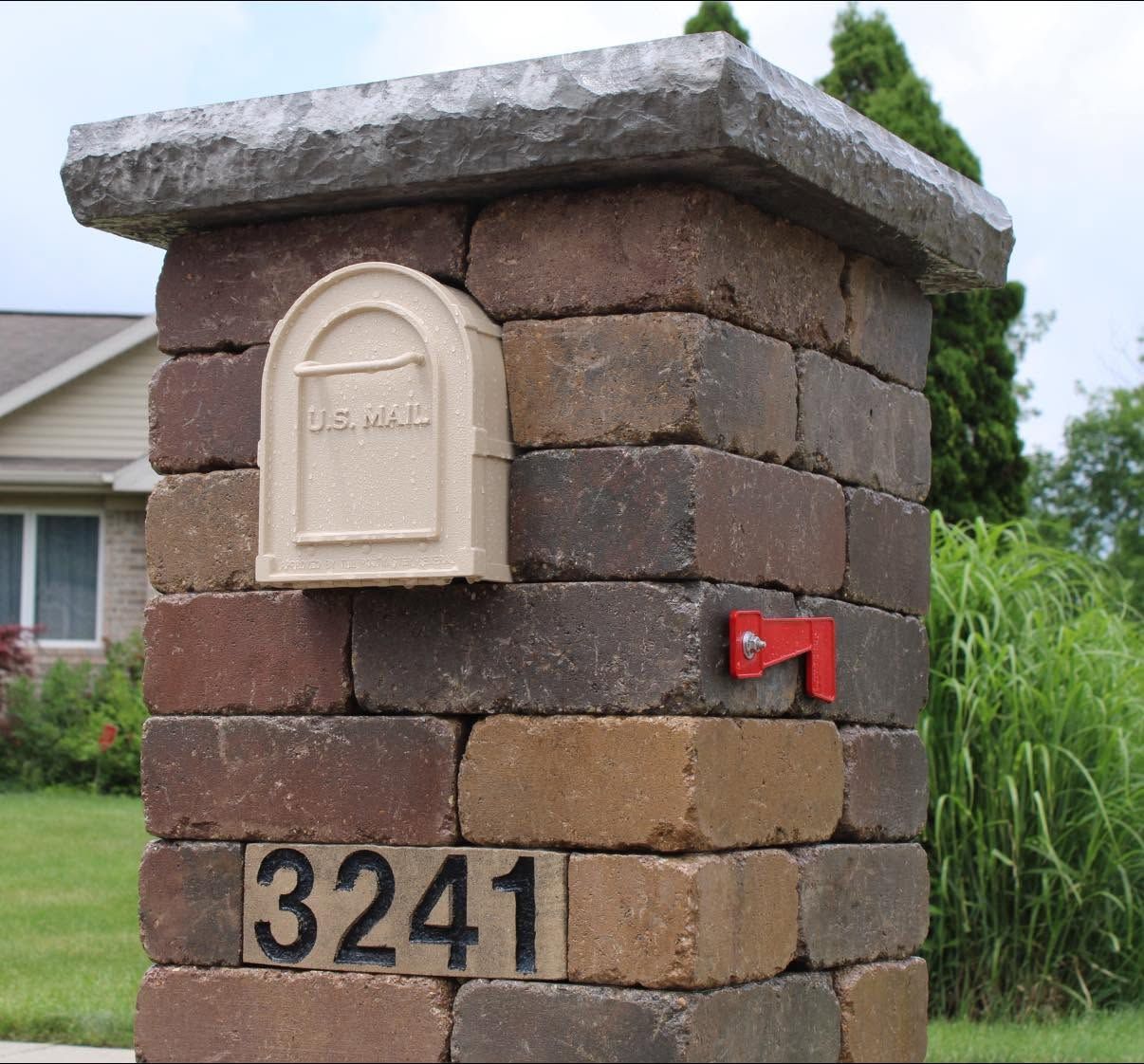 Brick mailbox with house number 3241 and a red flag outside a home