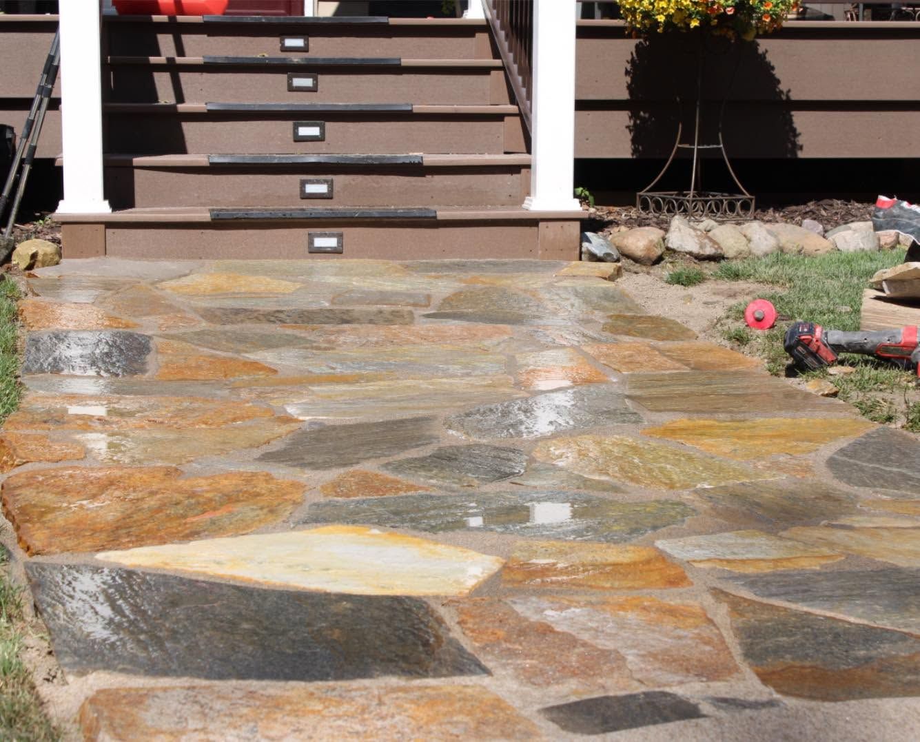 Stone walkway leading to front steps of a house with flower beds on the side