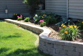 Curved stone garden border with blooming flowers beside a house and green lawn