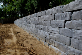 Stone retaining wall beside a sandy path, with trees and a wooden fence in the background.
