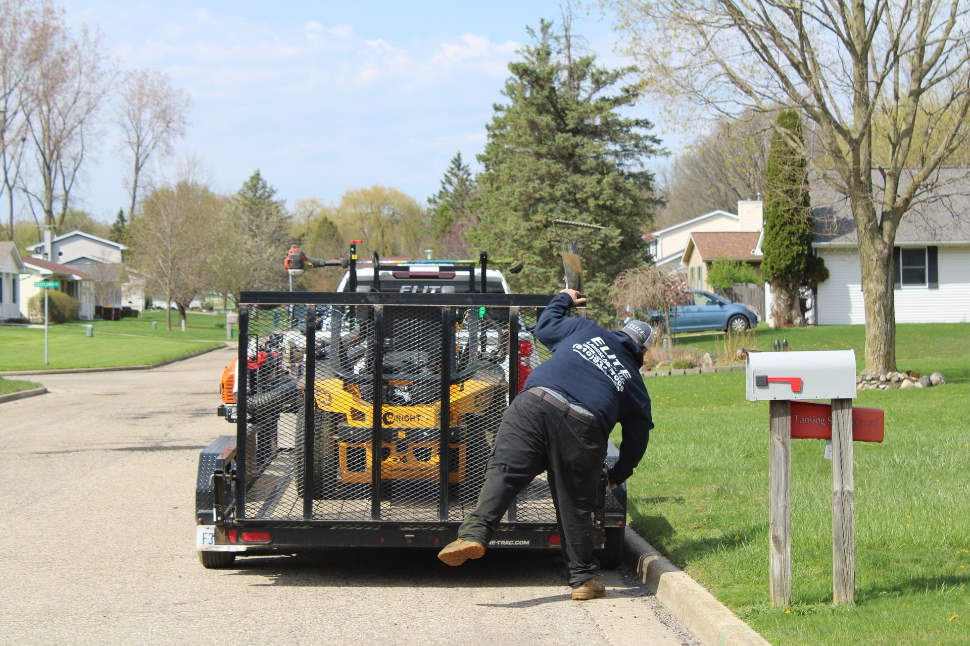 Worker loading yellow equipment into truck on a suburban street beside a mailbox