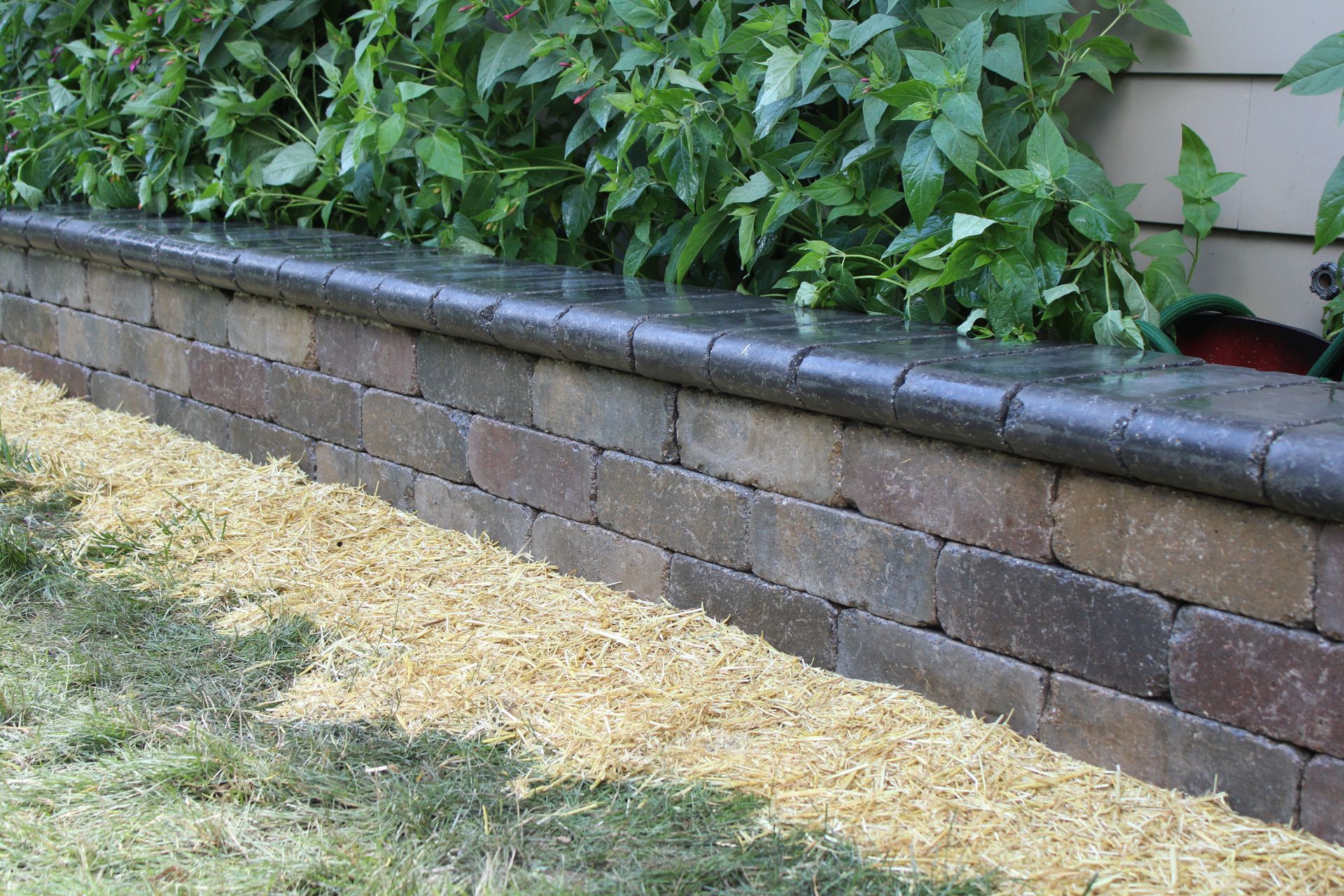 Raised brick garden wall with gray capstone beside mulch and green shrubs