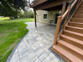Backyard patio with metal chairs, table, and grill beside a house and flower planters.