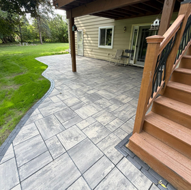 Backyard patio with metal chairs, table, and grill beside a house and flower planters.