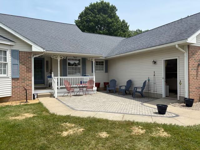 Patio with chairs and a table outside a brick-and-beige house, viewed from the backyard