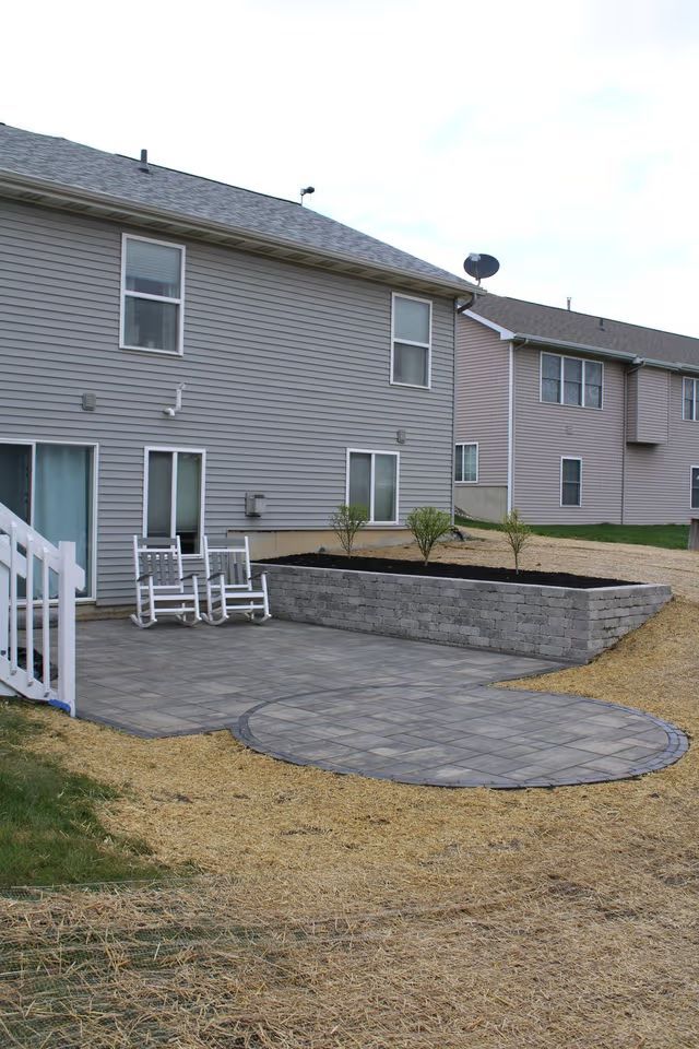 Backyard patio with stone pavers and raised planter beside beige townhouse homes