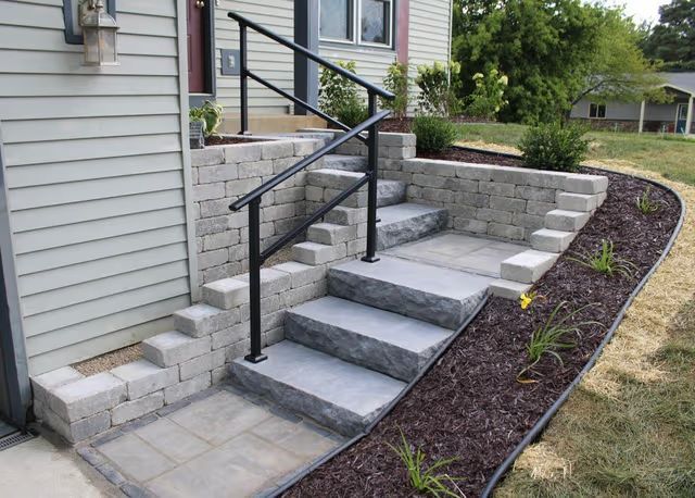 Front steps with black handrails and stone retaining walls leading to a house entrance.
