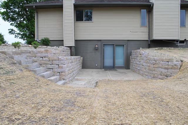 Backyard retaining walls and steps leading to a basement patio door beneath a house