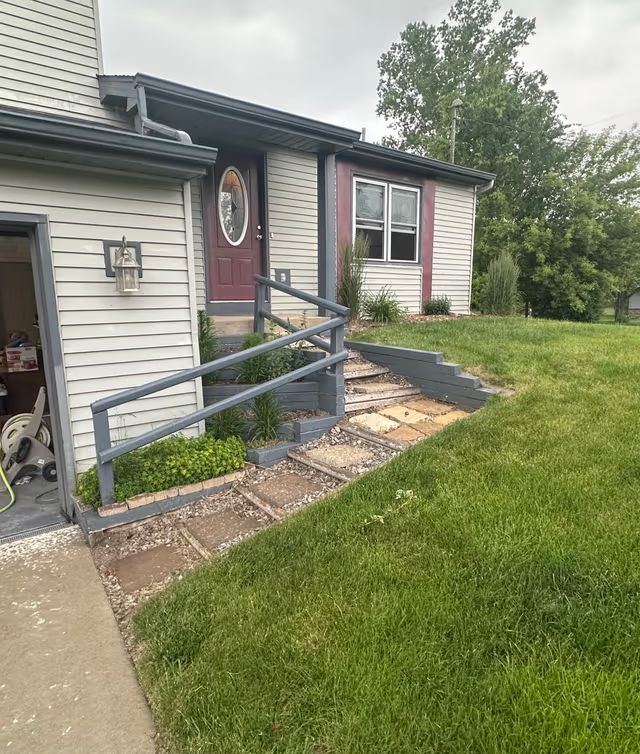 Front entrance of a house with a ramp, steps, and a stone walkway beside a grassy yard.
