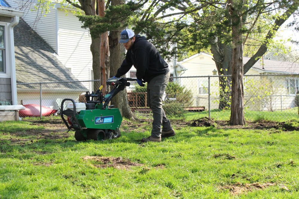Person using a green lawn aerator in a backyard beside trees and a house