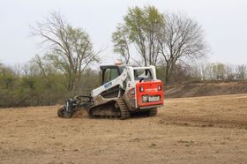 White Bobcat skid steer grading a dirt lot with trees in the background