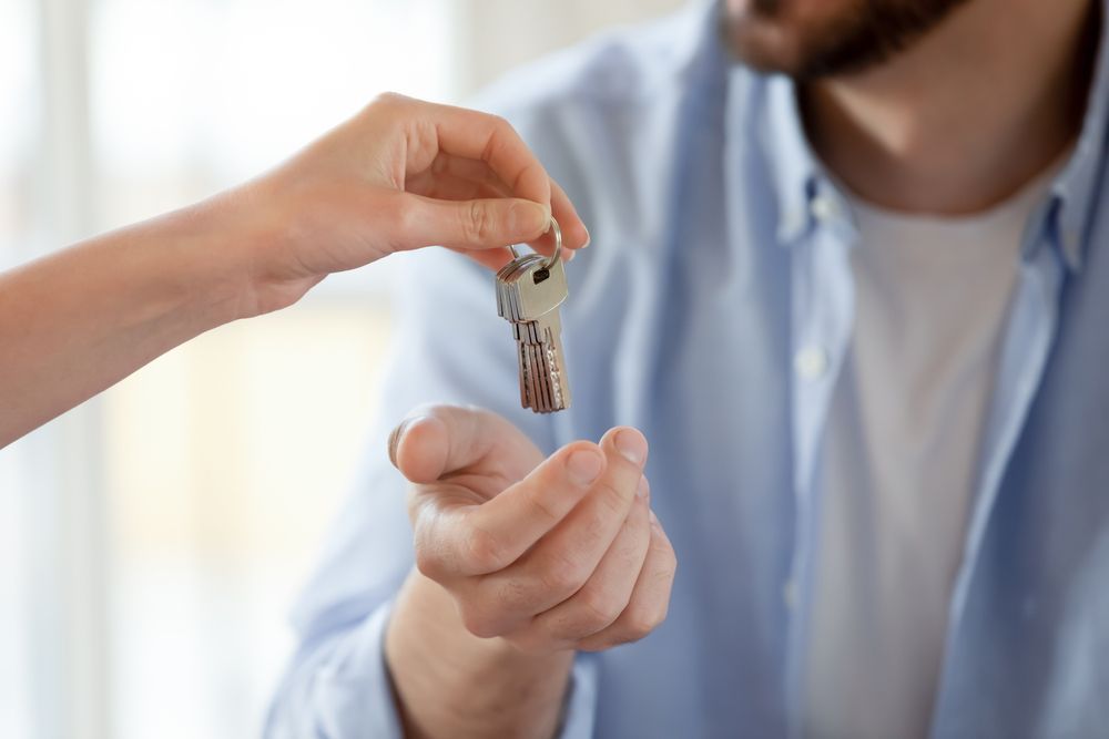 Handing Over a House Key from One Person to Another in A Bright Indoor Setting — Terrace Locksmiths in Belmont, NSW