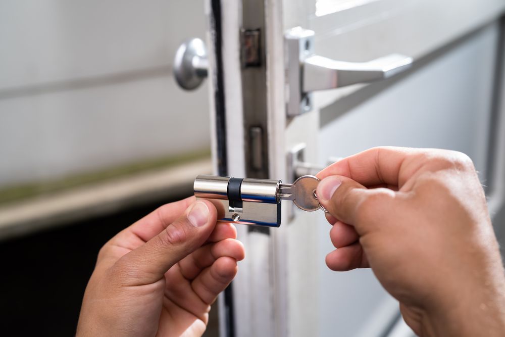 Hands Unlocking a Silver Door Latch with A Key — Terrace Locksmiths in Raymond Terrace, NSW