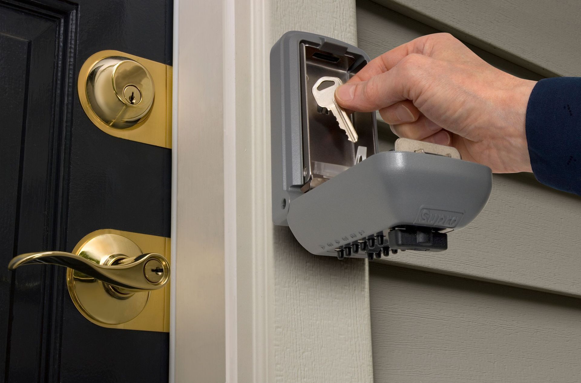 Hand using a key at a house door lock with a grey key lock box attached — Terrace Locksmiths in Raymond Terrace, NSW